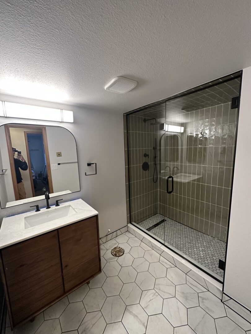 A bathroom with a sink, mirror and shower.